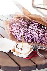 Bento cake with a candle with a bouquet of pink gypsophila on a wooden table, in a cafe. Little surprise for a girl's birthday
