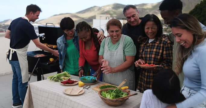 Multi generational people doing barbecue during weekend day at home's rooftop preparing vegetable food - Multiracial friends having fun cooking together - Summer and food concept