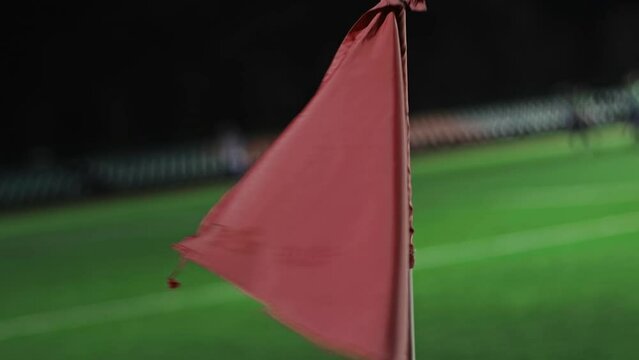 Red flag flutters in the wind in corner kick zone during soccer match at night. Slow motion. Close up. English football game in small stadium. Sport concept