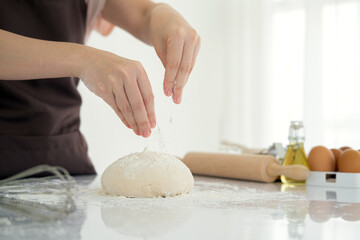 Beautiful and strong women's hands knead the dough sprinkling piece of fresh dough with flour make bread, pasta or pizza in white bright kitchen. chef hands with flour in a freeze motion .Copy space.