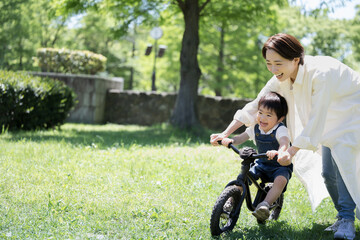 Parent and child practicing bike riding Leisure in a fresh green park Mom and boy Copy space left