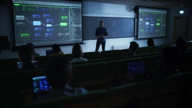 Young Male Lecturer Giving a Web Development Masterclass to Diverse Multiethnic Group of Female and Male Students in Dark College Room. Projecting Slideshow with Initial Programming Project Plan