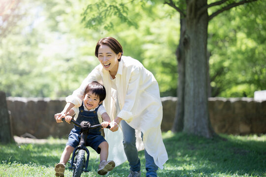 メインビジュアルにも！自転車の練習をする親子　新緑の公園でレジャー　ママと男の子　コピースペース右