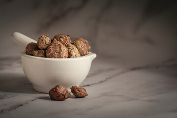 Closeup of Dry Spectacular Eulophia or Eulophia ochreata or Tubers of Amarkand (Eulophia nuda) fruits, in white ceramic mortar and pestle. Front view on marble background.