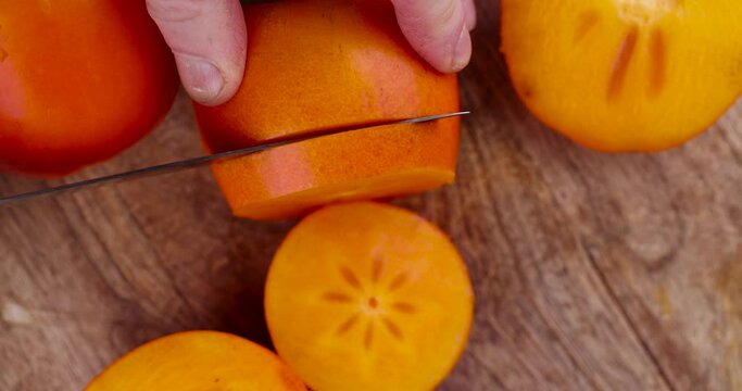 Half-ripe orange persimmon, fresh ripe persimmon cut into pieces on a cutting board with a sharp knife
