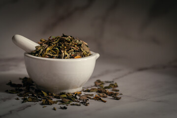 Closeup of Dry  Adulsa (Justicia adhatoda) leaves, in white ceramic mortar and pestle. Front view on marble background.