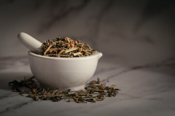 Closeup of Dry Ashwagandha (Withania somnifera) leaves, in white ceramic mortar and pestle. Front view on marbel background.