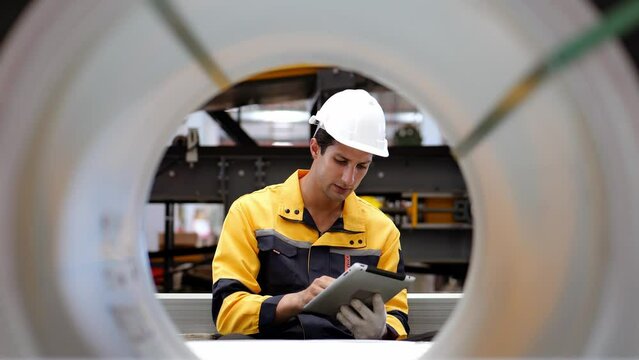 4k slow motion, Happy latin worker wearing safety uniform workwear, use tablet online information to check a stock of rolled steel sheets stored in warehouse factory to be produced as metal sheets.