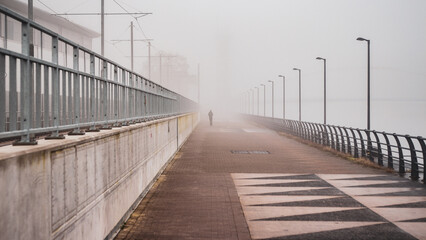 Obraz premium A silhouetted person walks down a misty path in an urban setting