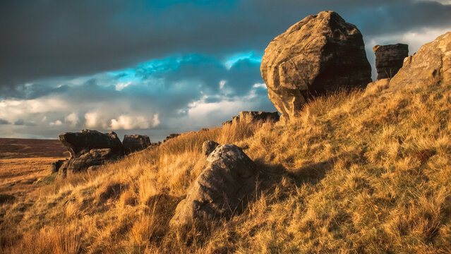 Sunset landscape of large rocks on a golden hillside against a cloudy sky