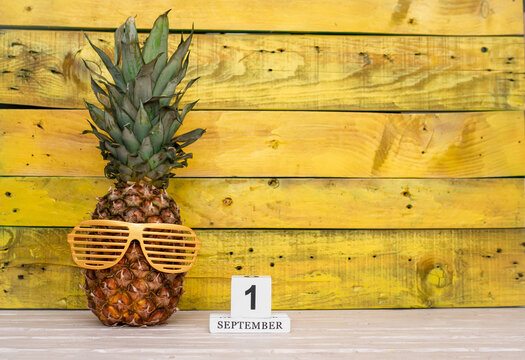Creative september calendar planner with number  1. Pineapple character on bright yellow summer wooden background with calendar cubes.