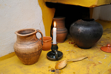 Traditional Ukrainian tableware clay ewer, pot, wooden spoon and burning candle placed near old...