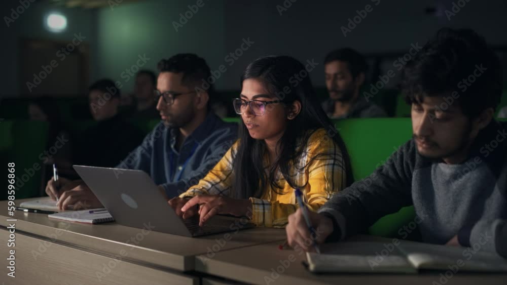 Poster Portrait of a Smart Talented Indian Female Student Studying in University with Diverse Multiethnic Classmates. Young Woman Using Laptop Computer and Taking Notes During the Lecture