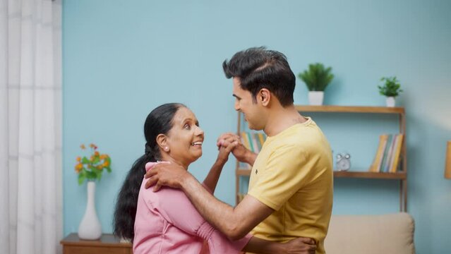 Happy Indian adult son with elderly active mother dancing by signing together at home - concept of generation, entertainment and playful retirement lifestyle