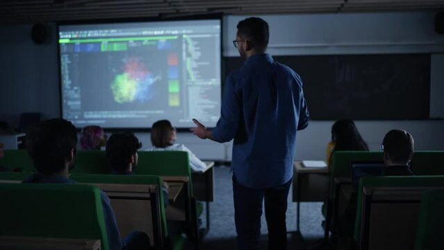 Young University Professor Explaining the Importance of Artificial Intelligence to a Group of Diverse Multiethnic Students in a Dark Auditorium. Teacher Walking Between the Rows While Giving a Lecture