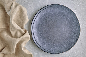 An empty gray ceramic plate and a rough linen napkin on a gray concrete table. Background for displaying food