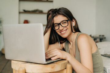 A young smiling woman surfs the internet from home using a laptop.