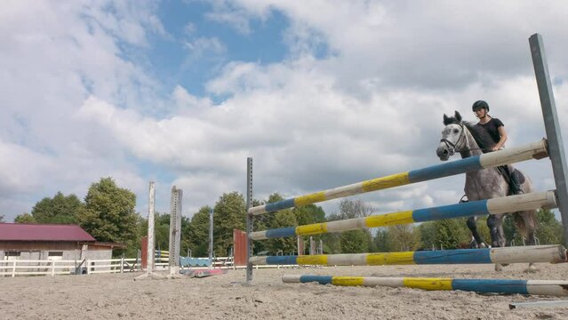 Female jockey leaping hurdles on her trained horse during preparation for showjumping competition, low angle view.