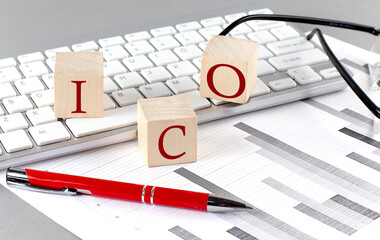 ICO written on a wooden cube on the keyboard with chart on grey background