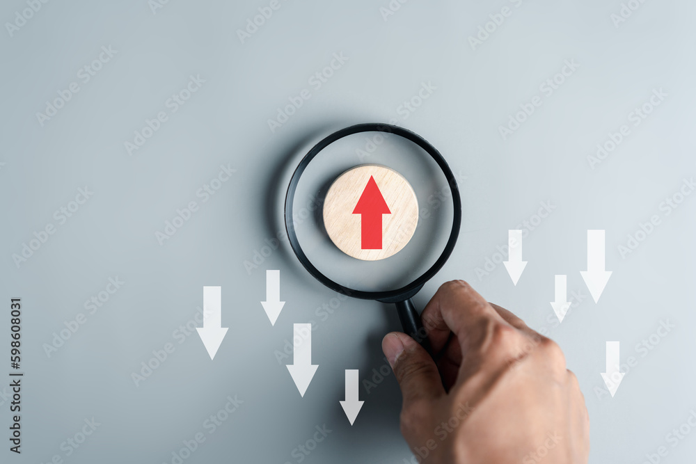 Fototapete Hand holding magnifier focus to Red arrow and different direction facing opposite direction with white arrow for business disruption and technology transformation and different thinking idea concept.