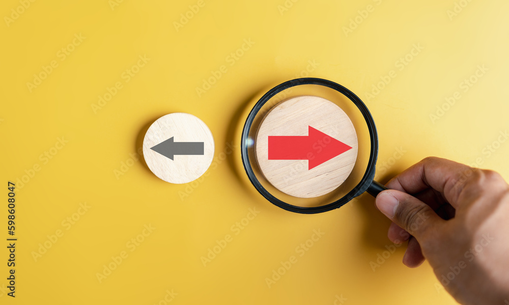 Fototapete hand holding magnifier focus to red arrow and different direction facing opposite direction with bla