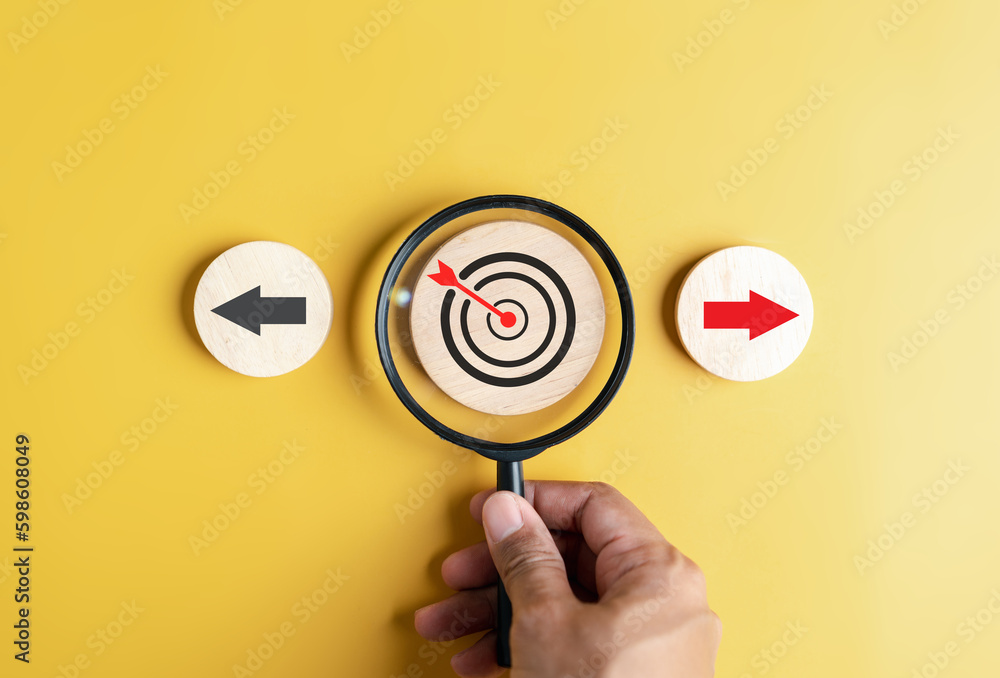Aufkleber Hand holding magnifier focus to dardboard with Red arrow and different direction facing opposite direction with black arrow for business disruption and technology transformation.