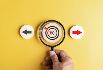 Hand holding magnifier focus to dardboard with Red arrow and different direction facing opposite direction with black arrow for business disruption and technology transformation.