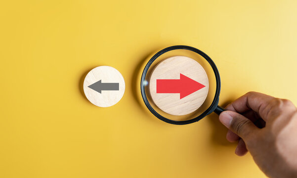 Hand holding magnifier focus to Red arrow and different direction facing opposite direction with black arrow for business disruption and technology transformation and different thinking idea concept.