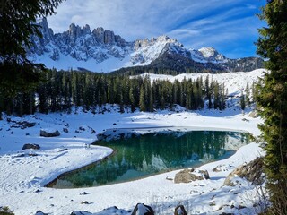 
Karersee or Lago Carezza with snow capped mountains in the background and reflected in the water, surrounded by lush green pine trees
