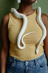 Cropped shot of young African American woman with white rat snake creeping over her on neck and...