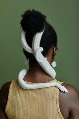 Back view of young African American woman with white rat snake enlacing her hair bun standing in...