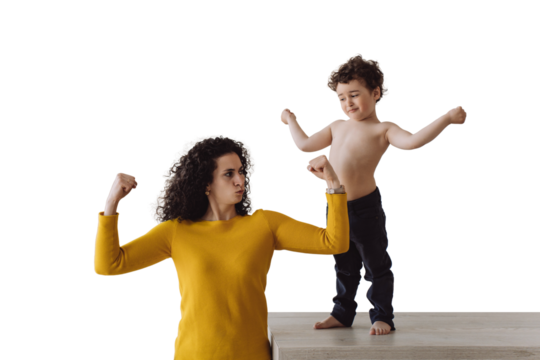 Sporty caucasian curly woman at kitchen with son demonstrating her biceps and curly son standing on table showing biceps. Italian young babysitter spending time with kid against transparent background - Powered by Adobe