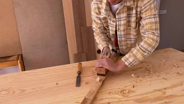 Handy man flattening wood plank with jack plane. Happy male woodworker looking at camera and smiling while smoothing wooden detail