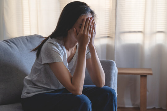 Asian woman covering her face feeling sorrow and depressed sit in the dark bedroom