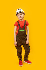 Full-length portrait of teenage boy in white protective helmet and work overalls on yellow background. Vertical frame.