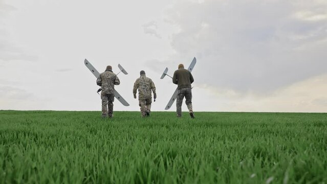 Ukraine Circa spring 2023 - Three soldiers are preparing to launch drones in a field. The military pilots are walking with aerial vehicles in their hands.