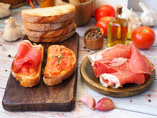 Tapas and ingredients on a wooden board. Toasts with tomatoes and ham