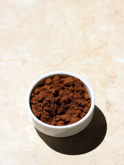 Roasted ground coffee in a small ceramic white bowl on a light marble table on a sunny morning. Close up of roasted ground coffee isolated on a light marble background with copy space for text