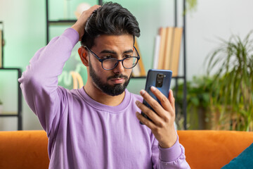 Sad displeased indian man use smartphone typing browsing, loses becoming surprised sudden lottery...