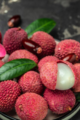 Juicy Lychee with cut in half and leaves on plate on a dark background, top view
