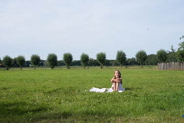 A girl sitting outside in a wide open field on a hot summer day during a vacation
