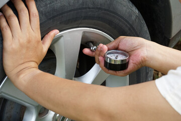 Woman checking the pressure of an old car tire with a tire pressure gauge for safety and assurance before use.