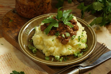 Puree with meat sauce and herbs on a wooden background