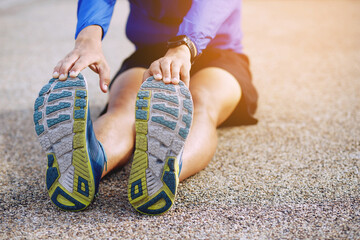 young man runner stretching for warming up before running or working out on the road. Track and Field Athlete exercise. Fitness and sport healthy lifestyle concept. copy space banner.