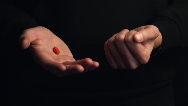 Studio shot male hands show red pill then blue pill isolated on black background. Concept of making right choice. Cinematic 4K footage