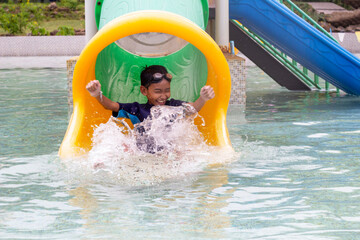 Asian little boy playing water slide at water park having fun on summer vacation.