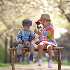 Zwei Kinder sitzen auf einer Bank mit roter Rose