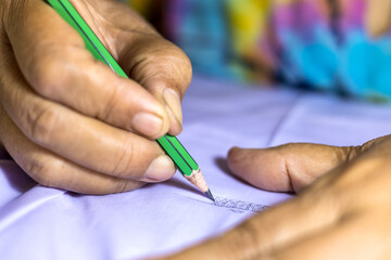 Close-up low view of elderly female hand holding a pencil to write letters on a white.