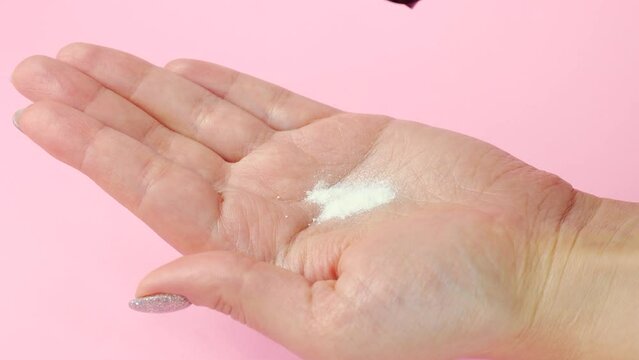 White enzyme powder pouring into the Caucasian woman hand from the bottle close up. Skin care and facial cleansing
