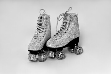 Pair of glitter silver stylish roller skates on gray background. Black and white photo.